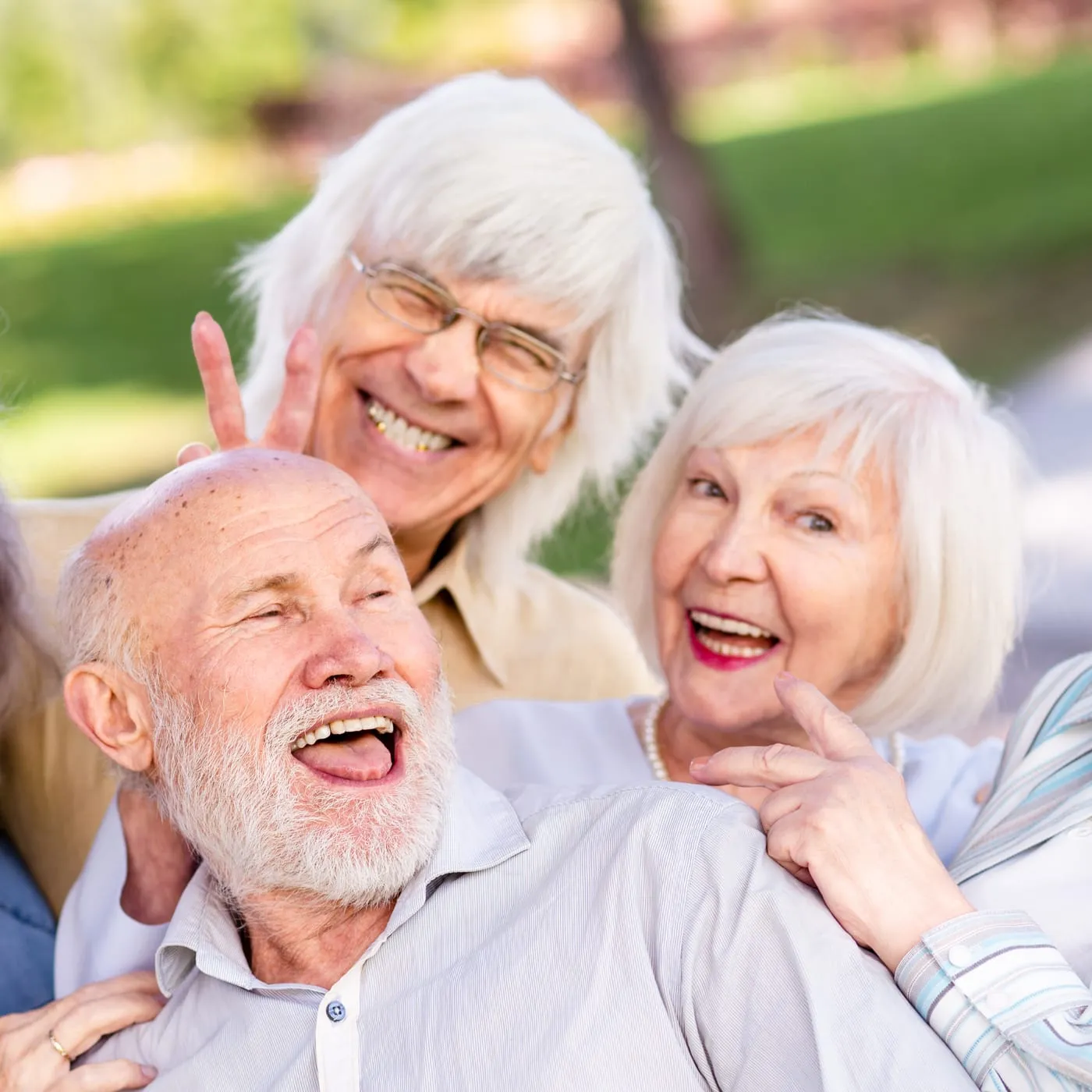 Drei ältere Menschen lachen ausgelassen miteinander im Grünen