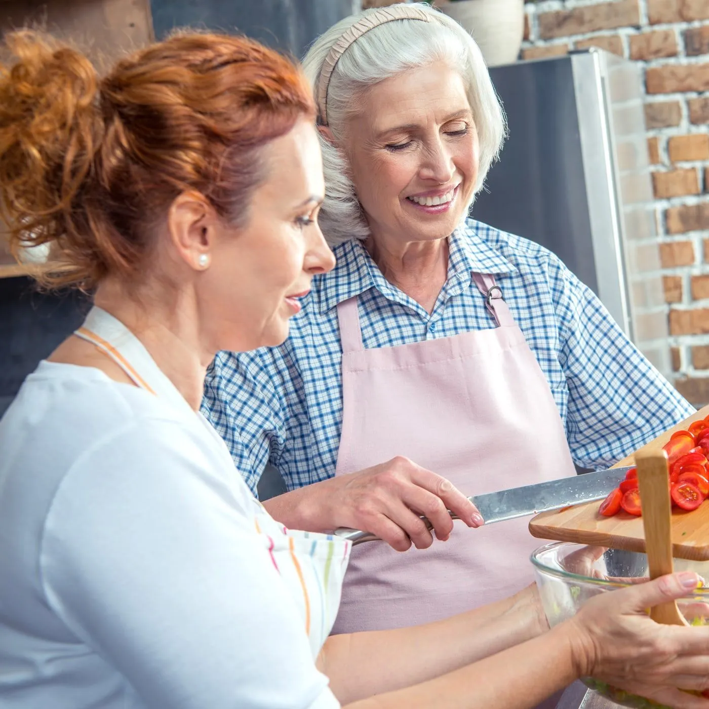 Eine Seniorin und eine jüngere Frau bereiten gemeinsam in der Küche einen Salat zu und lächeln
